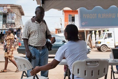 Woman holds chair out, offering good customer service to a low-income customer at a prototype financial services business in Accra, Ghana