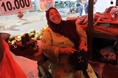 Entrepreneur laughs in her place of business - a fruit stall. Low-income earners like this woman require financial services tailored to their business and personal financial needs – and delivered in a user-friendly, customer-centric approach.