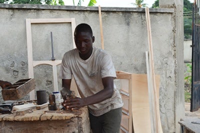 Carpenter saws wood in Kumasi, Ghana. Low-income individuals like this man seek financial predictability and reliable income but may face challenges and risks that prevent them from achieving these goals 
