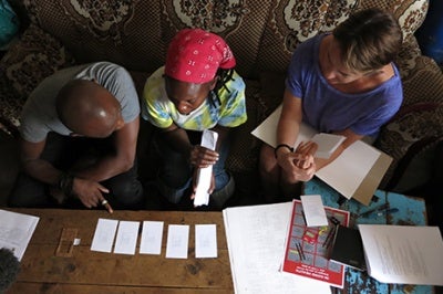 Low-income woman in Kenya looks at papers on table during a one-on-one customer insights qualitative research interview in her home.