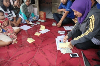 Low-income women in Indonesia look at and discuss their microcredit group loan documents 