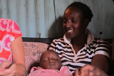 Low-income woman in Kenya smiles and holds baby during a qualitative interview in her home. 