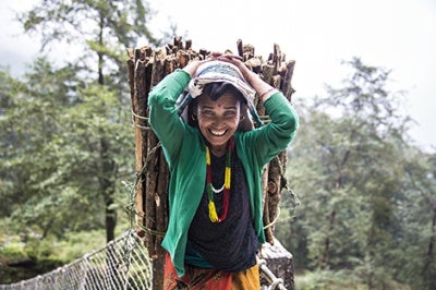Woman smiles as she carries wood. Low-income customers and those with less stable income flows like this woman in rural Nepal benefit from financial services and products that suit their needs and behaviors, and make formal financial services more accessible and intuitive for low-income segments.